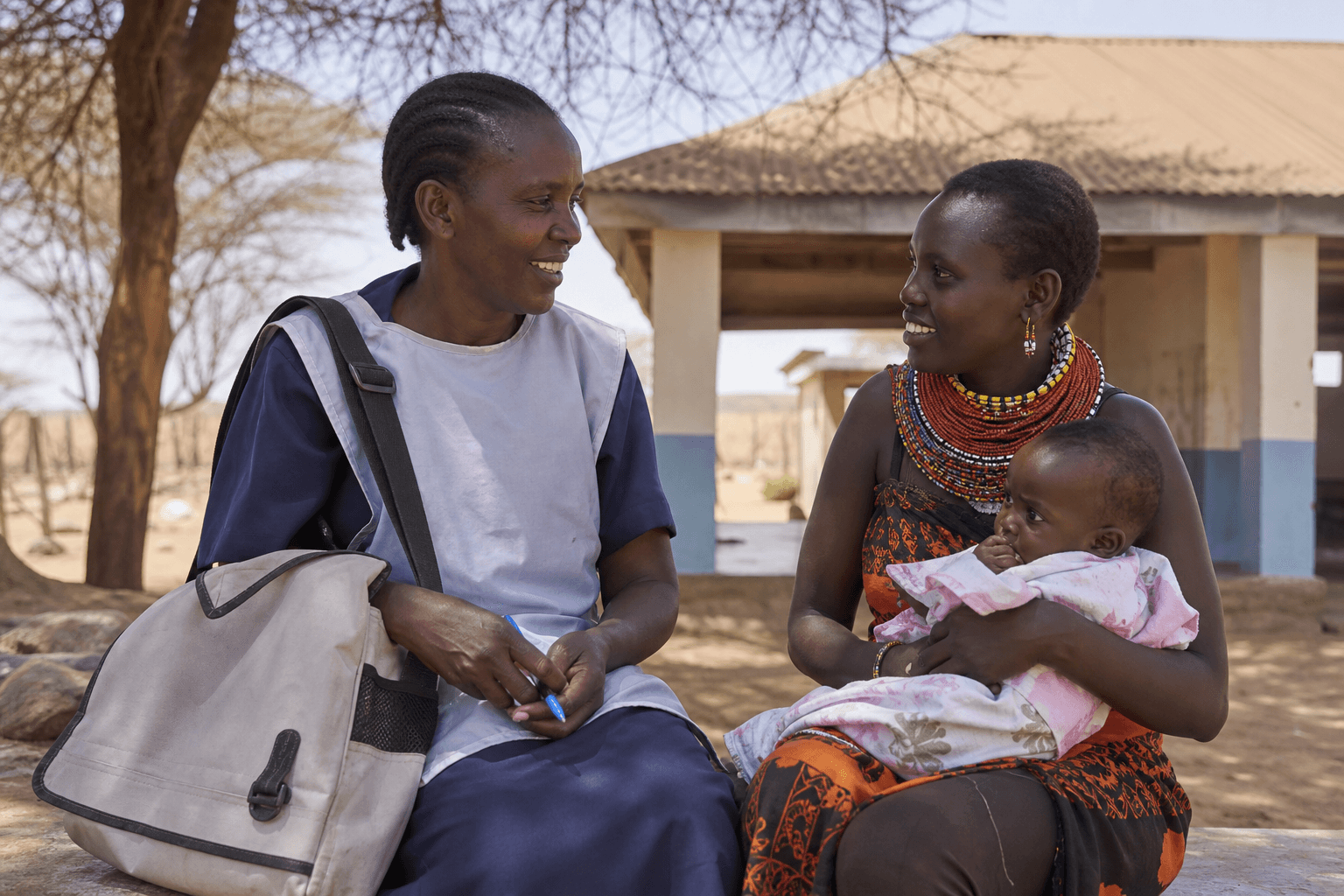 A community health volunteer with a supply kit talking with a mother outside a rural clinic, Samburu County